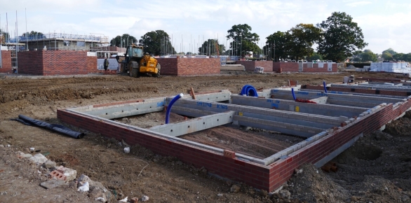 Concrete foundation with brick walls and installed plumbing pipes on a construction site.