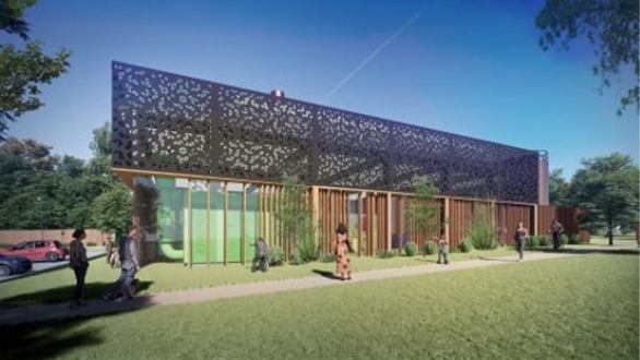 A modern building with a perforated, decorative upper facade, wooden vertical panels on the lower level, surrounded by green grass and trees, with people walking along a paved pathway in front.