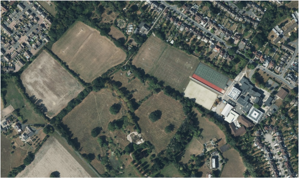 Aerial photograph of land at and surrounding Arden Academy school showing mix of small fields with hedgerows and scattered trees, and leafy mature suburb housing.